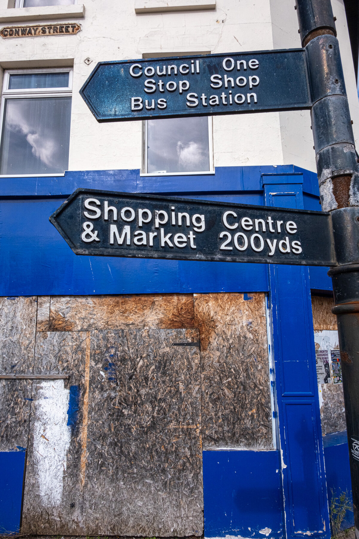 Directional signage mounted above a boarded blue shopfront
