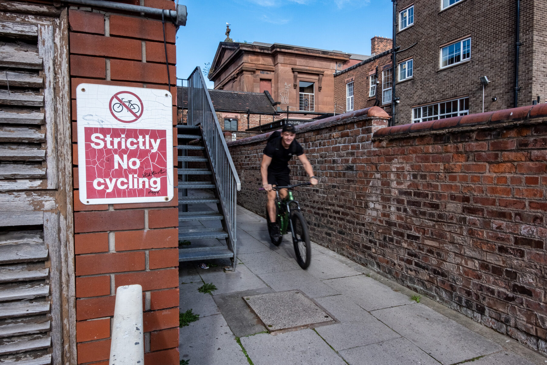 Cyclist riding down steps directly past a strictly no cycling sign
