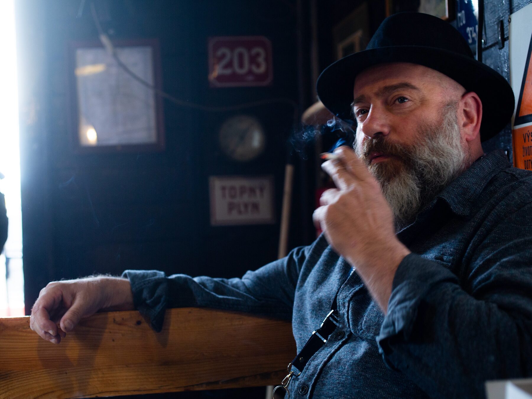 Glen Emery in a Prague pub, hat and cigarette, beneath old Czech enamel signs