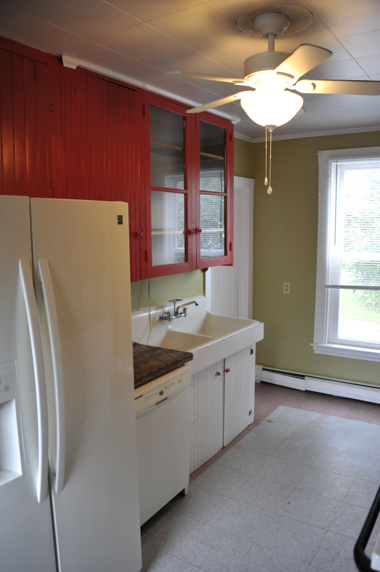 The kitchen corner with fridge, sink and lit ceiling fan
